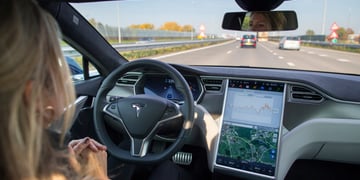 blue sky, inside of car, road ahead ,female blonde driver, tesla car, T on driving wheel, big screen