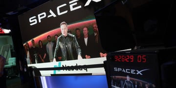 spaceX logo, elon musk on big screen, taking in video, black jacket, nasdaq