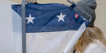 voting machine, blue and two white stars, blonde hair, dark grey beany hat, white jumper