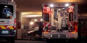 ambulance bay by hospital, two white ambulance cars, one with back door open, light blue seat