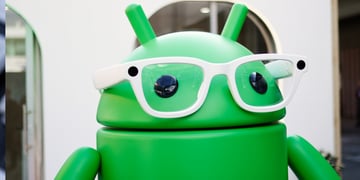 Green stylized Google Android mascot, white frame glasses, black eyes, alien ears
