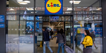 lidl store, glass wall and door, white woman in padded yellow winter jacket, shopping cart 