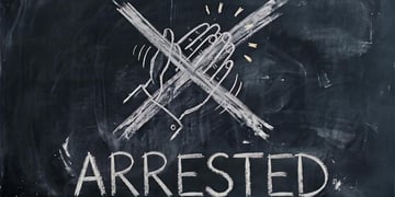A chalkboard with clapping hands drawn and crossed out, the word "arrested"