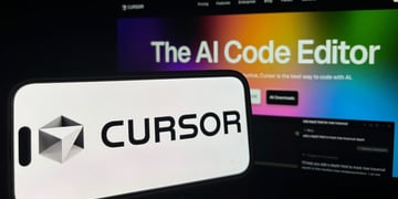 Cursor logo on phone, background AI coding agent written on computer screen.