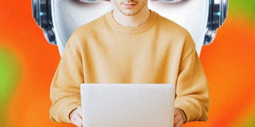 A person sitting at their laptop, big robot's head behind it