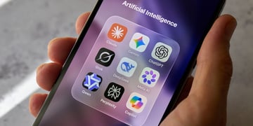 A hand holds a smartphone displaying the Claude, Gemini, ChatGPT and other AI apps