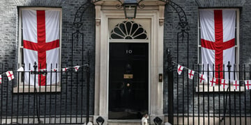 cat sits on doorstep, number 10 on door , flags in windows