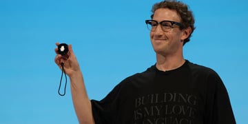 Zuckerberg, curly hair, black tshirt, baby blue background, small round gadget in raised right hand