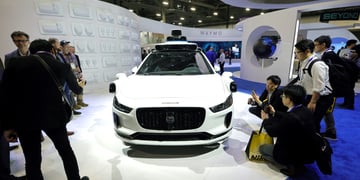 white Jaguar car on white pedestal, people around in black outfits take pictures of it 