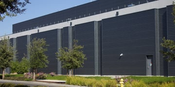 dark grey ai data centre building, some green grass, blue sky, five trees