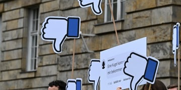 Protesters in Germany stand with their Facebook thumbs pointing down posters