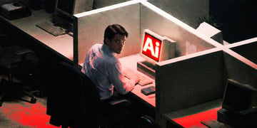 Man sitting in front of PC saying "AI", and looking back, mischief in his face, in dark office