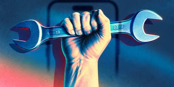A hand holding a wrench with a smartphone in the background