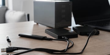 External hard drives, a portable SSD and USB cables connect to a laptop on a wooden desk