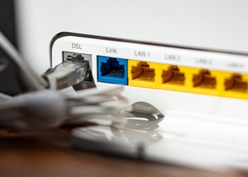 A grey LAN cable is plugged into the grey DSL slot of a white WLAN router, yellow, blue slots