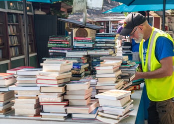 old man, live yellow reflective vest, blue tshirt, piles of books, shelves of books, tan, brown shorts