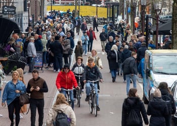 busy street filled with white pedestrians, cyclists, red jacket, water canal, blue jeans jacket