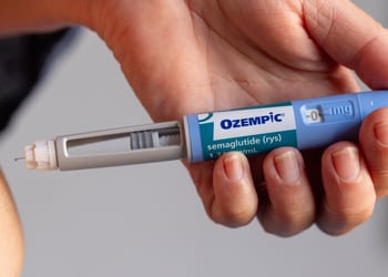 white person belly, white hand, baby blue ozempic pen, grey wall