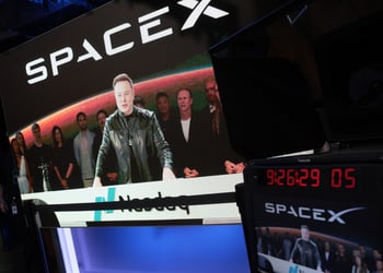 spaceX logo, elon musk on big screen, taking in video, black jacket, nasdaq