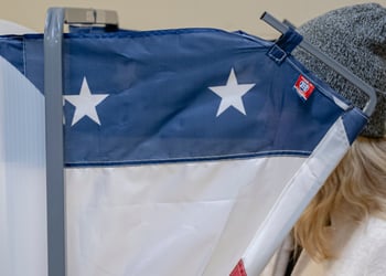 voting machine, blue and two white stars, blonde hair, dark grey beany hat, white jumper
