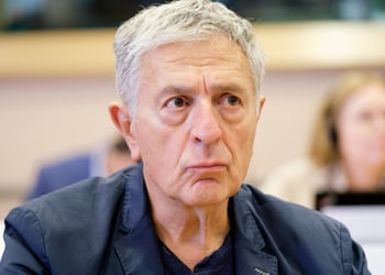 Stelios Kouloglou, white elder greek man, black collar shirt, no tie, grey hair, dark blazer,