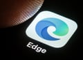 microsoft edge blue-greenish icon in white background on black screen, finger tip