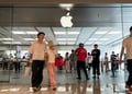 middle aged white asian couple exit apple store, logo, pink pants, black hair, glass wall, white tshirt