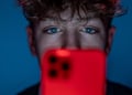 teen boy, curly hair, red smartphone, dark blue room, blue eyes