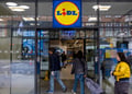 lidl store, glass wall and door, white woman in padded yellow winter jacket, shopping cart 