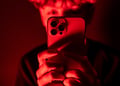 teenage boy looks at an iPhone screen displaying various social media apps in red background