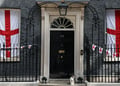 cat sits on doorstep, number 10 on door , flags in windows